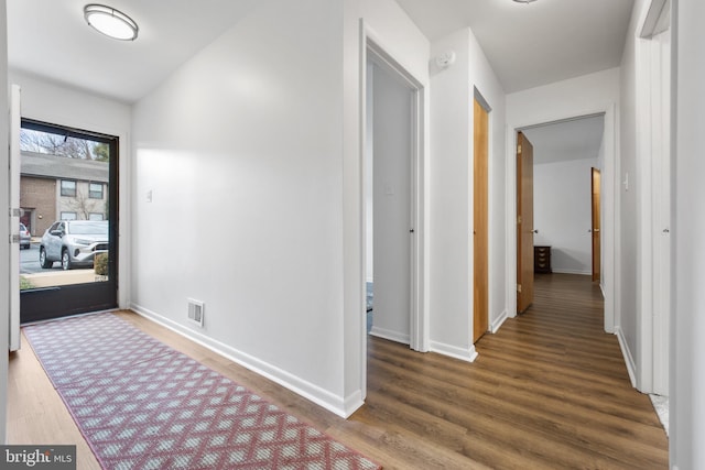 hall with baseboards, visible vents, and wood finished floors