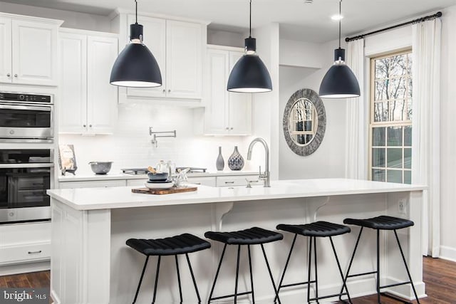 kitchen with a center island with sink, appliances with stainless steel finishes, dark wood-style flooring, light countertops, and white cabinetry