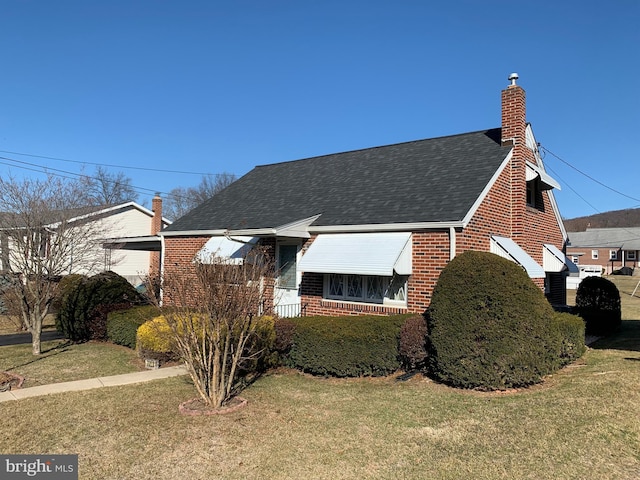 view of front of property with brick siding, a chimney, a front yard, and a shingled roof