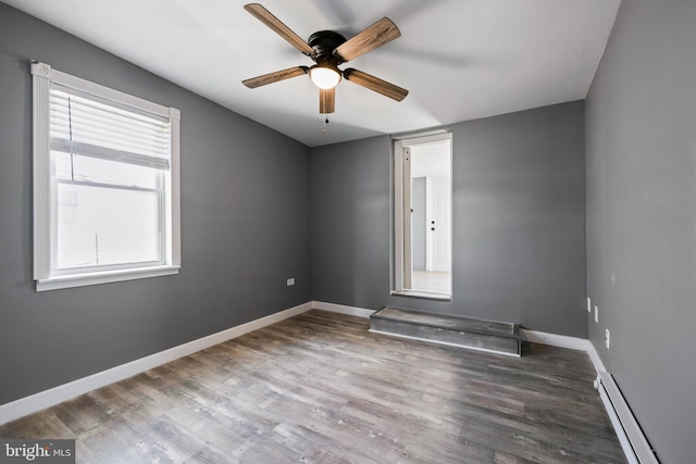 unfurnished room with a baseboard heating unit, a ceiling fan, baseboards, and wood finished floors