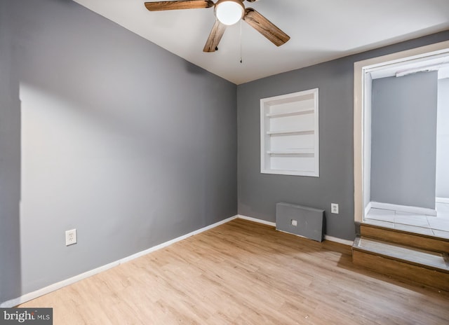 unfurnished room with a ceiling fan, built in shelves, baseboards, and wood finished floors