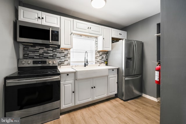 kitchen with a sink, white cabinets, light countertops, appliances with stainless steel finishes, and light wood finished floors