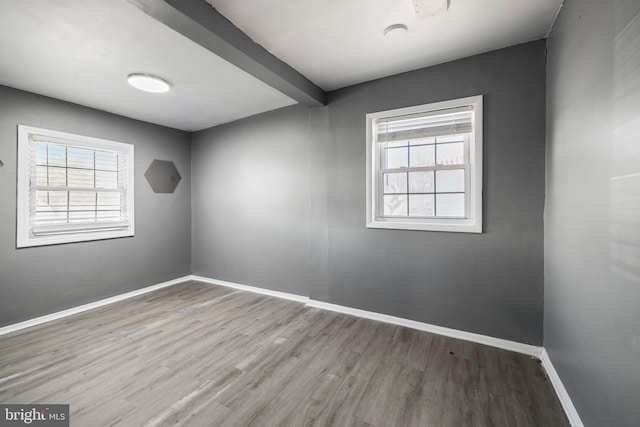 spare room with plenty of natural light, beamed ceiling, baseboards, and wood finished floors