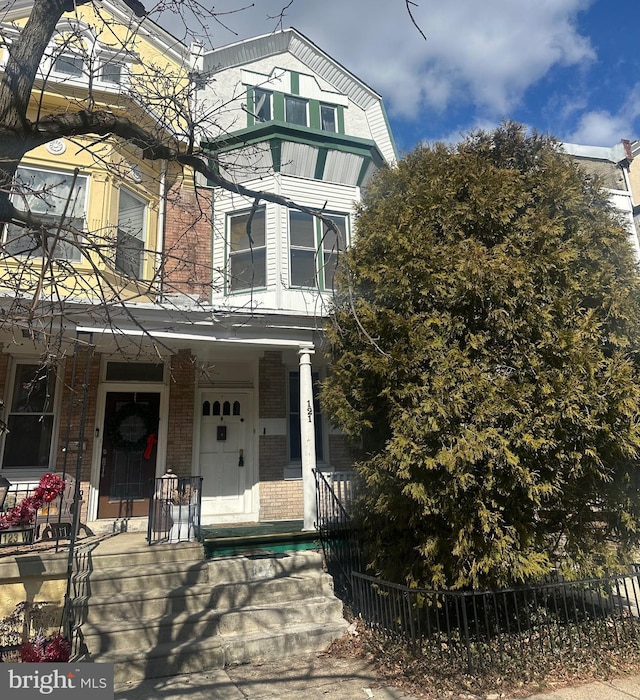 view of front of property featuring covered porch, brick siding, and a fenced front yard