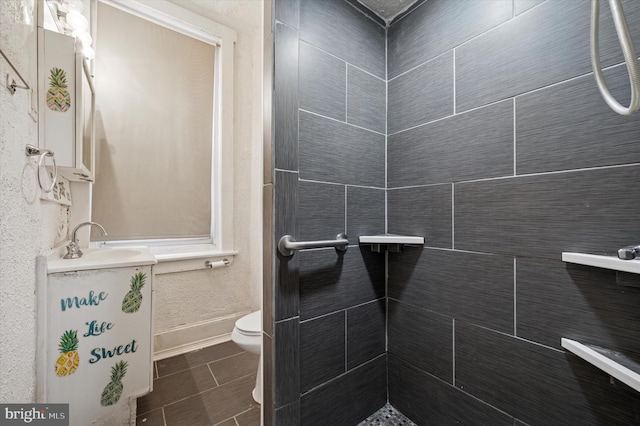 full bathroom featuring toilet, tiled shower, vanity, and baseboards