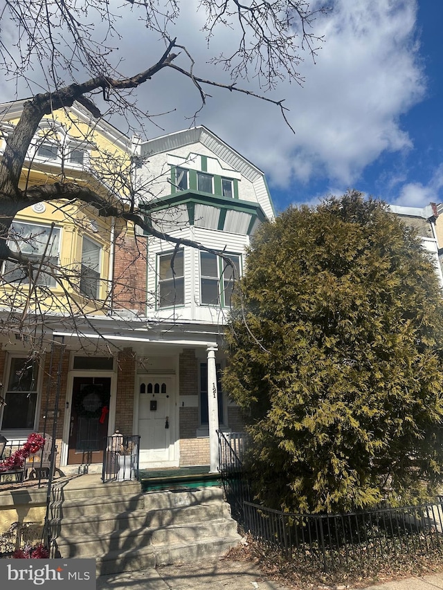 view of front of house featuring a porch, brick siding, and a fenced front yard