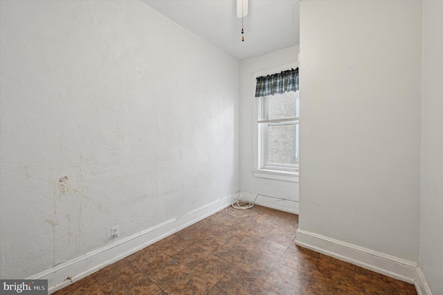 unfurnished room featuring ceiling fan, stone finish flooring, and baseboards