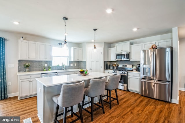 kitchen featuring stainless steel appliances, dark wood-style flooring, white cabinetry, light countertops, and a center island