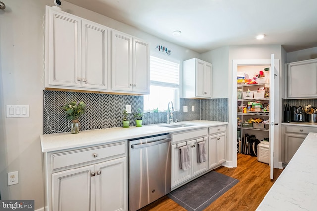 kitchen featuring light countertops, decorative backsplash, stainless steel dishwasher, a sink, and wood finished floors