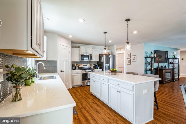 kitchen with a breakfast bar area, stainless steel appliances, dark wood-style flooring, a sink, and white cabinets