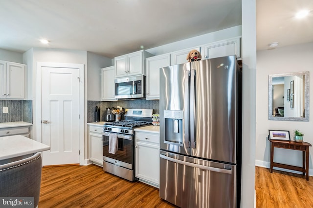 kitchen featuring stainless steel appliances, light countertops, backsplash, and wood finished floors