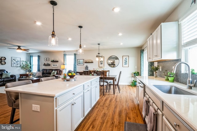 kitchen with a sink, white cabinetry, light wood-style floors, hanging light fixtures, and backsplash