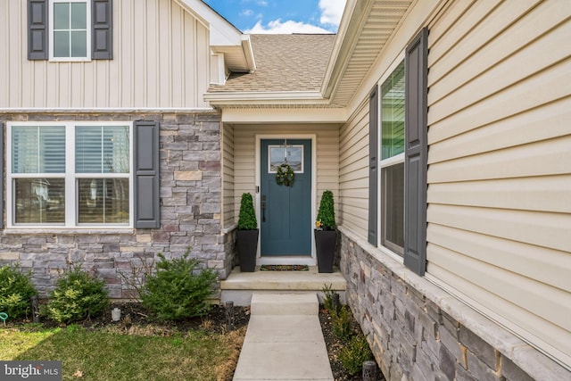 entrance to property featuring board and batten siding, stone siding, and roof with shingles