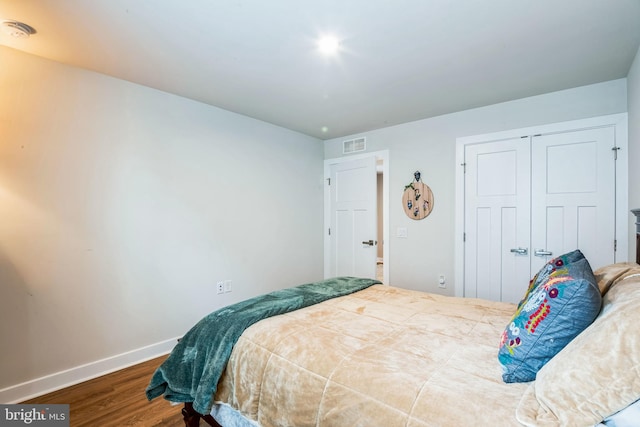 bedroom with a closet, visible vents, baseboards, and wood finished floors