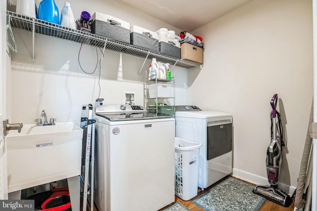 clothes washing area featuring laundry area, baseboards, light wood-style flooring, washing machine and dryer, and a sink