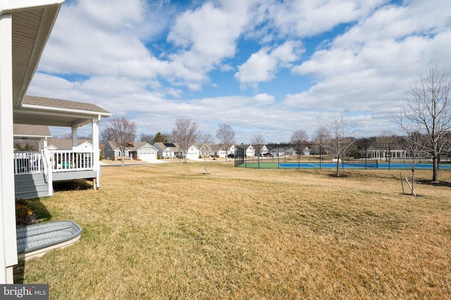 view of yard featuring a tennis court, fence, and a residential view