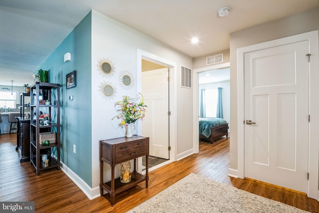 hall with baseboards, visible vents, and wood finished floors