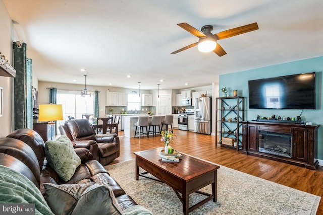 living area with recessed lighting, ceiling fan, wood finished floors, and a glass covered fireplace