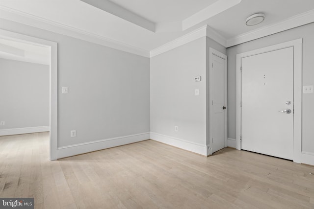 empty room with ornamental molding, a raised ceiling, baseboards, and light wood finished floors