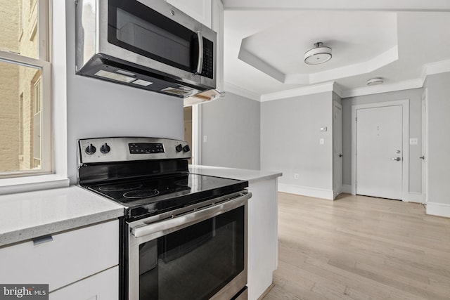 kitchen featuring light wood-style flooring, white cabinets, ornamental molding, appliances with stainless steel finishes, and a tray ceiling