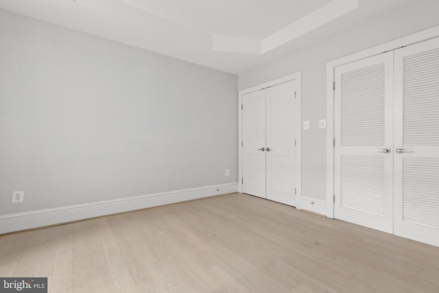 unfurnished bedroom with light wood-style flooring, baseboards, a raised ceiling, and multiple closets