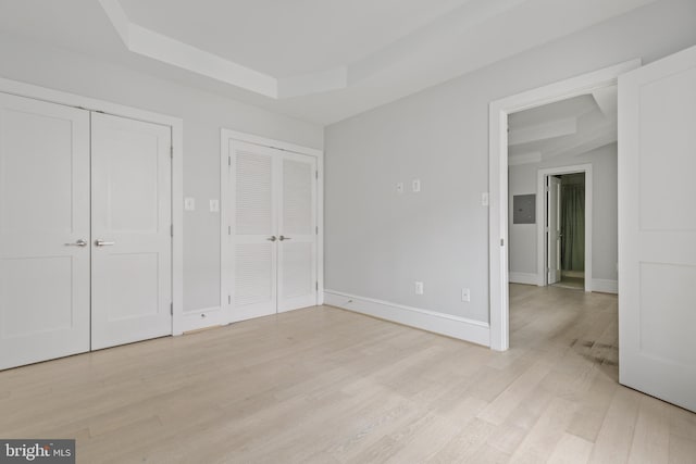 unfurnished bedroom featuring baseboards, a tray ceiling, light wood-style flooring, and multiple closets