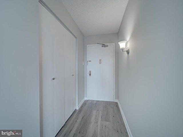 hallway with light wood finished floors, baseboards, and a textured ceiling