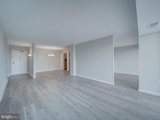 unfurnished living room with a textured ceiling, light wood-style floors, visible vents, and an inviting chandelier