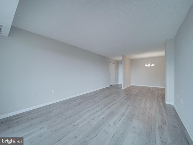 unfurnished living room featuring wood finished floors, a textured ceiling, baseboards, and an inviting chandelier