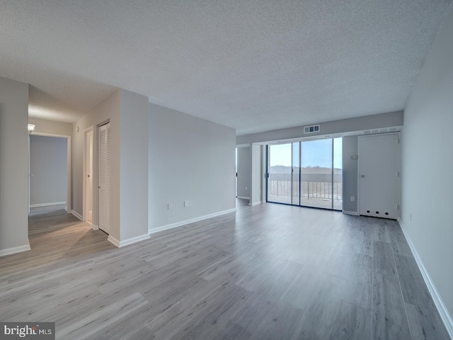 empty room with a textured ceiling, wood finished floors, visible vents, and baseboards