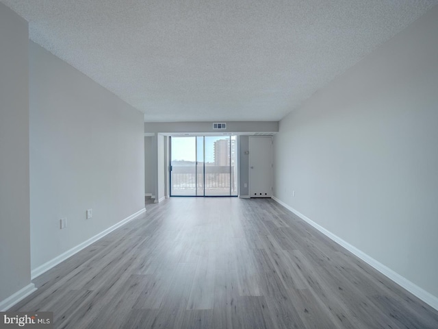 unfurnished room with a textured ceiling, baseboards, and wood finished floors