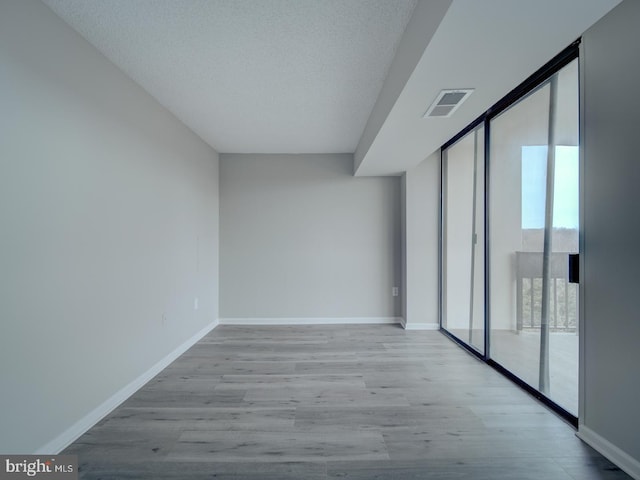 empty room featuring expansive windows, wood finished floors, visible vents, and baseboards