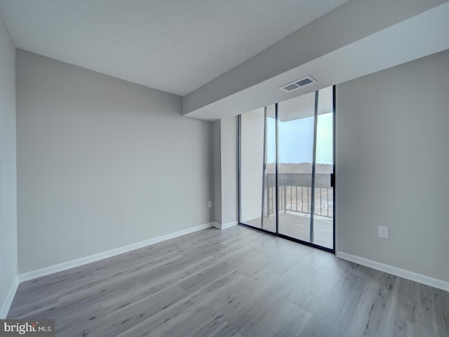 spare room with baseboards, expansive windows, visible vents, and wood finished floors