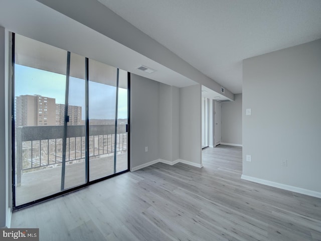 unfurnished room with baseboards, floor to ceiling windows, visible vents, and wood finished floors