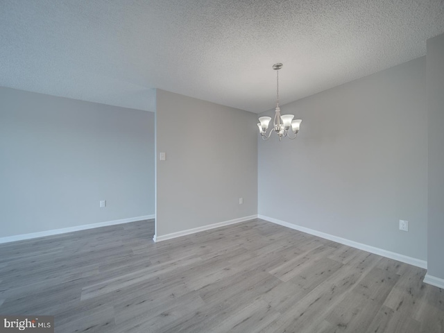 empty room with a notable chandelier, light wood-style flooring, and baseboards