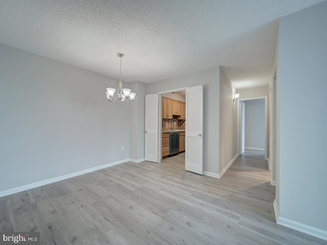 unfurnished dining area with light wood-type flooring, a notable chandelier, a textured ceiling, and baseboards