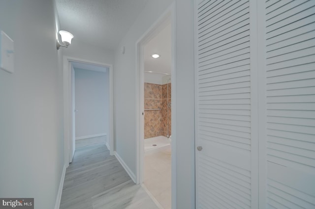 hallway with a textured ceiling, light wood-type flooring, and baseboards