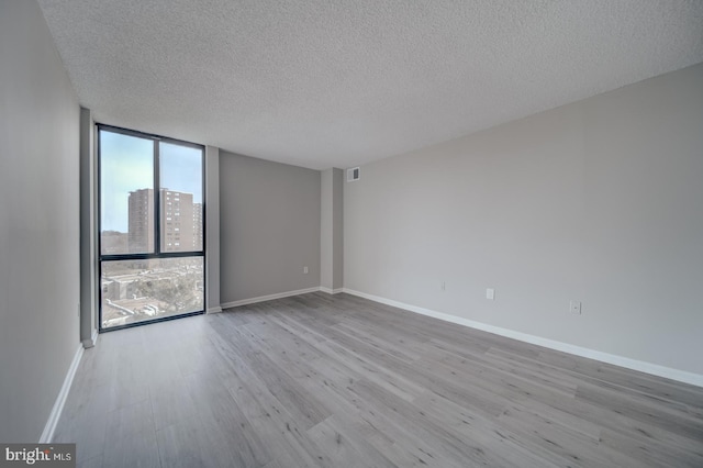 empty room featuring expansive windows, baseboards, and wood finished floors