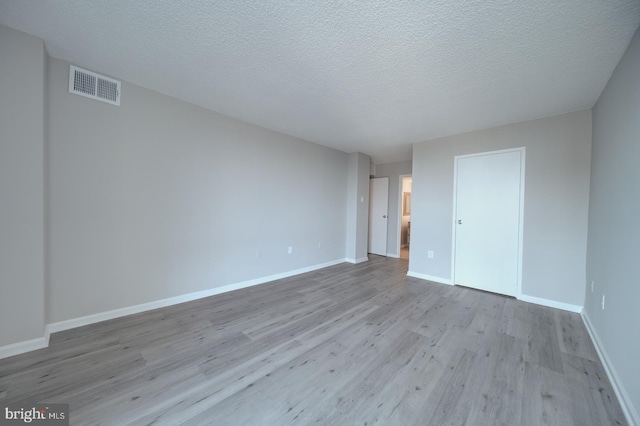 unfurnished bedroom featuring visible vents, a textured ceiling, baseboards, and wood finished floors