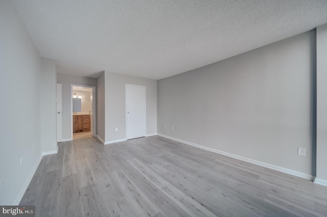 unfurnished bedroom featuring light wood finished floors, connected bathroom, baseboards, and a textured ceiling