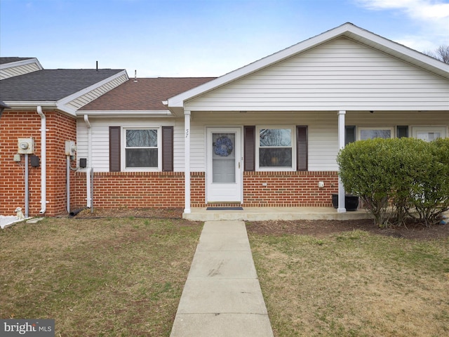 bungalow-style home featuring a front lawn, covered porch, brick siding, and a shingled roof