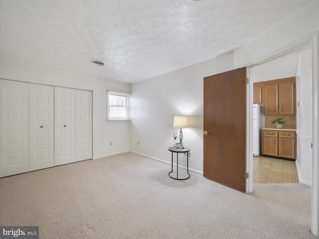 unfurnished bedroom with visible vents, light colored carpet, freestanding refrigerator, a closet, and a textured ceiling