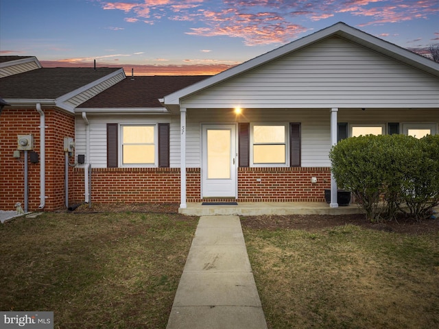 bungalow-style house with a yard, brick siding, covered porch, and roof with shingles