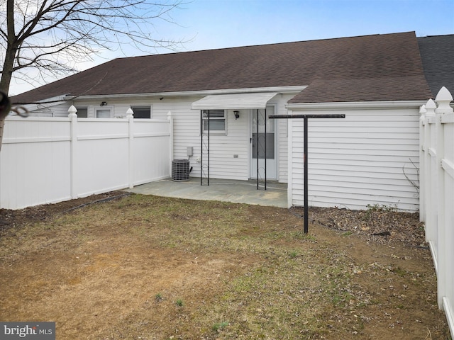 rear view of house featuring a shingled roof, fence, central air condition unit, a yard, and a patio