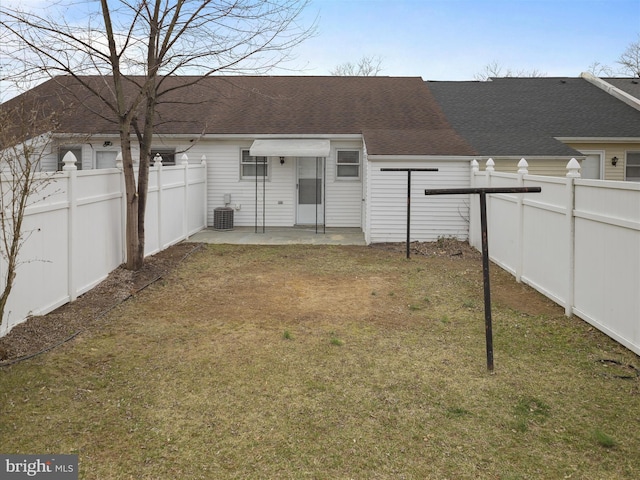 rear view of house with central AC unit, a lawn, a shingled roof, and a fenced backyard