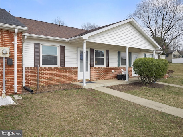 view of front facade with a front yard, covered porch, brick siding, and roof with shingles