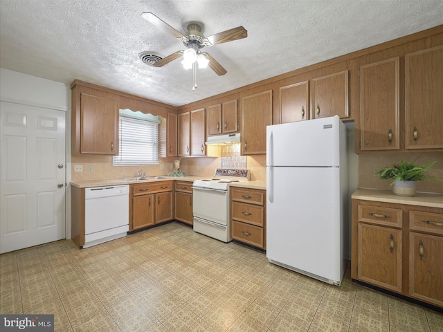 kitchen featuring ceiling fan, under cabinet range hood, light countertops, brown cabinetry, and white appliances