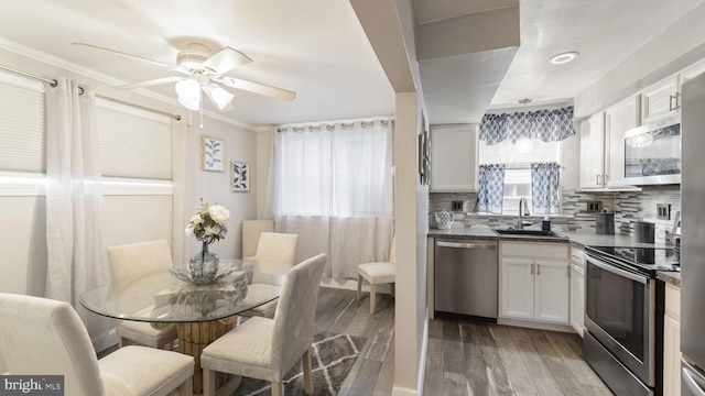 kitchen featuring stainless steel appliances, a sink, white cabinetry, light wood-style floors, and backsplash