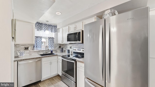 kitchen featuring white cabinets, decorative backsplash, stainless steel appliances, light wood-style floors, and a sink