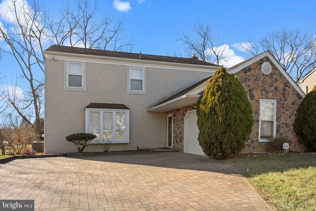 traditional home featuring a garage, stone siding, stucco siding, and central air condition unit